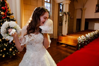 Lucie in a white wedding dress, standing in church next to a Christmas tree, laughing