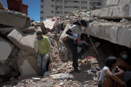 Woman amid wreckage wearing a dust mask and holding an electric drill