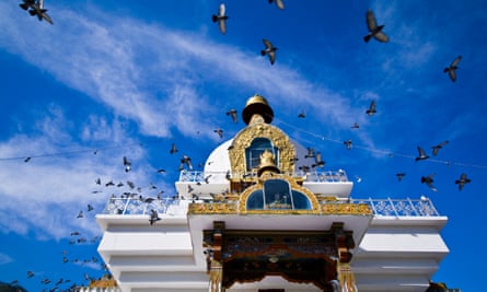 A flock of pigeons circle the golden spire of the Memorial Chorten beneath a blue sky.Thimphu Memorial Chorten, Thimphu Bhutan.