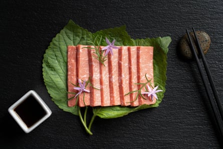 A dish of cell-cultured seafood, which looks like tuna, served on a leaf with a bowl of dipping sauce.