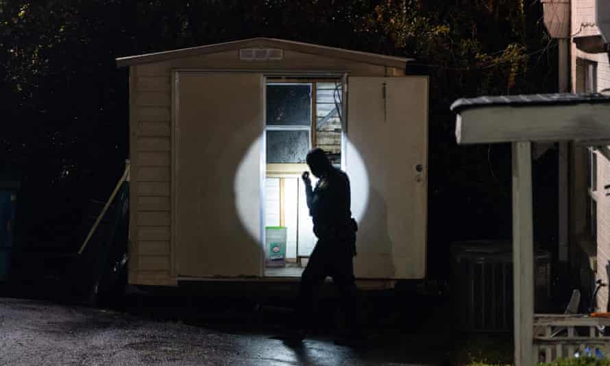A police officer uses a flashlight to look in a shed outside a massage parlor where three people were shot and killed on Tuesday in Atlanta, Georgia.