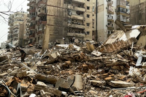 People inspect damage while stood on massive pile of rubble and debris from destroyed buildings.