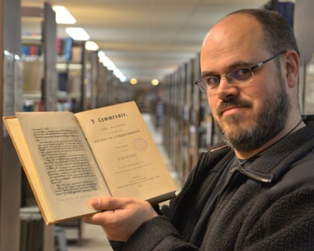 Dr Simon Rodway stands in a library holding up a copy of Y Cymmrodor (‘The Welshman’)