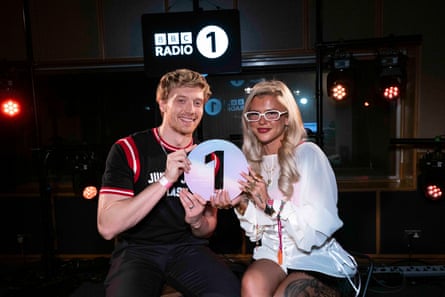 Skye Newman at the BBC Maida Vale Studios last December after performing for Radio 1’s Sound of 2026 live sessions. They are holding up a white disc with a large 1 on it, the radio station’s logo. Newman is wearing a white outfit and white-framed glasses