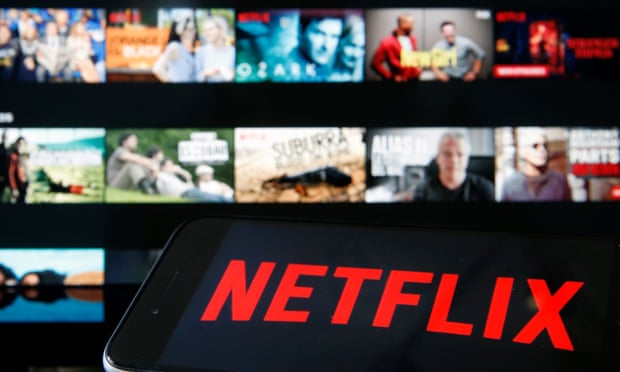 Netflix media service provider’s logo is displayed on the screen of an iPhone in front of a television screen
