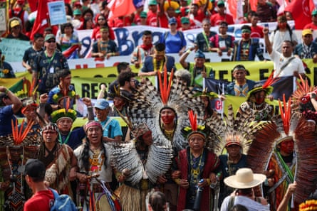 Protesters in traditional clothing and headdress hold banners outside Cop30 in Belém