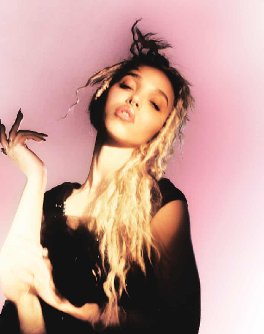 A portrait of FKA twigs with blond hair against a pink background
