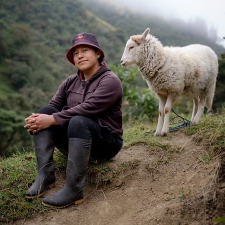A woman sits on a muddy slope next to a sheep.