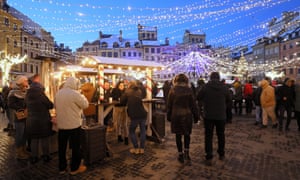 People visit Christmas market stands at the Old Town Square in Warsaw, Poland on 26 December. The lights twinkle against the pale blue sunset sky.