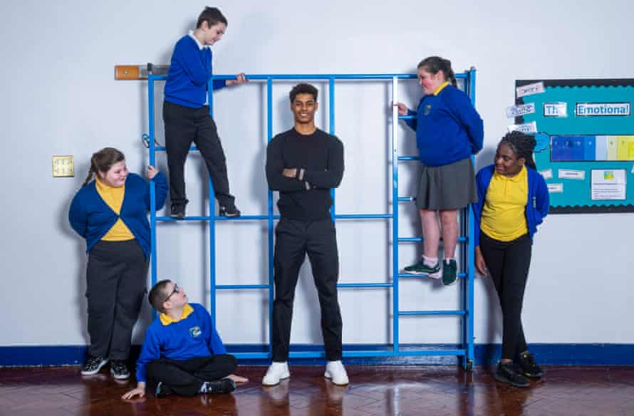Marcus Rashford standing in front of a climbing frame with pupils at his former primary school