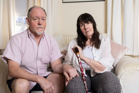 A man in a pink shirt sits with a woman on a sofa, both looking glum.