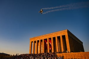 A fighter jet leaves white vapour trails behind it as it flies over a mausoleum flying a giant Turkish flag at its entrance