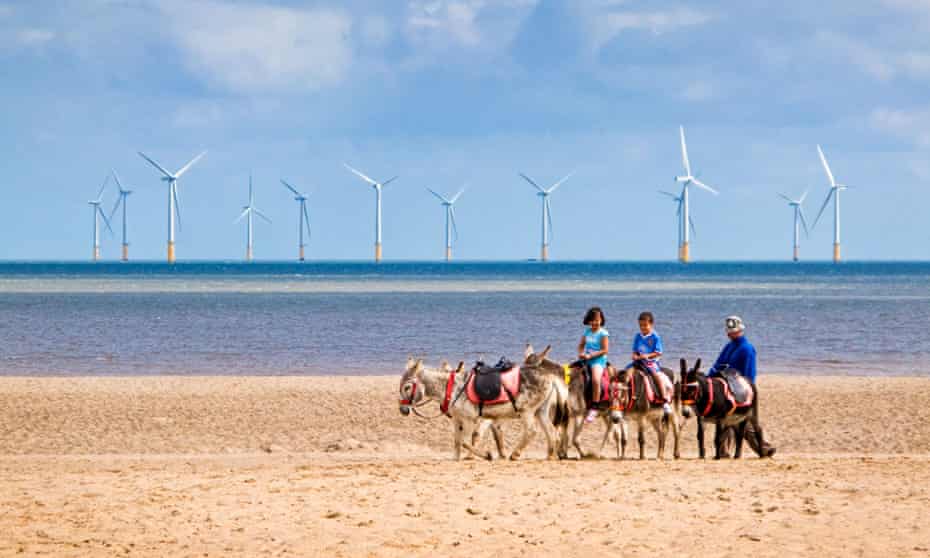 Children ride donkeys on Skegness beach with offshore wind turbines pictured in the background