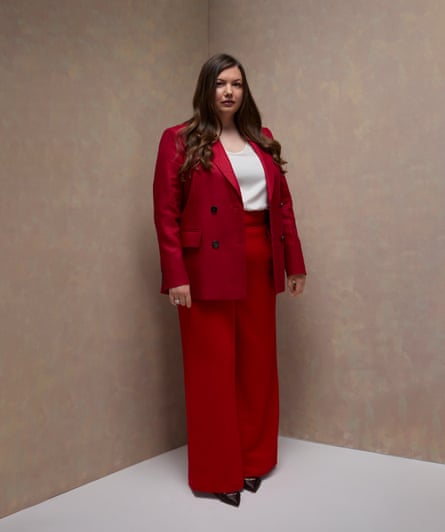 Hannah Murray wears a red blazer and red trousers with a white T-shirt and her long brown hair is worn down