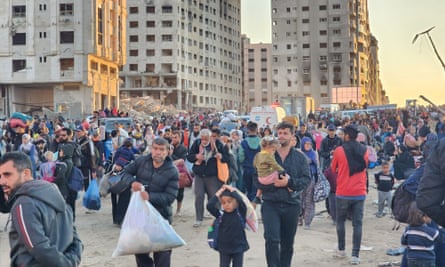 Crowd of people walking along a road alongside damaged buildings