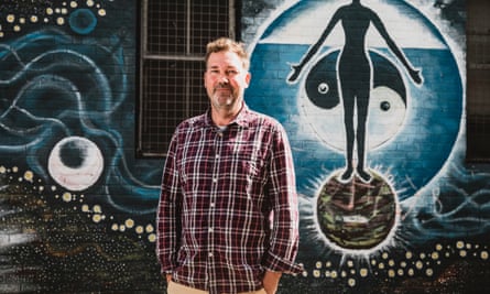 Hans Lovejoy, editor of Byron Bay newspaper The Echo, stands in front of a building with a new age mural painted on it