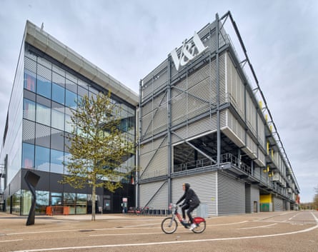 A man cycles past V&A East Storehouse, a modern metal and glass building.