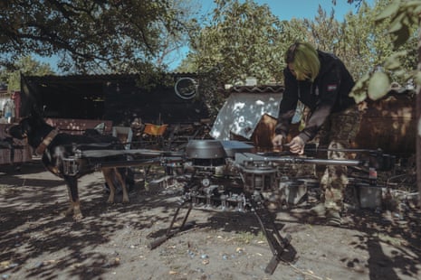 A woman with green bobbed hair adjusts something on a large black drone