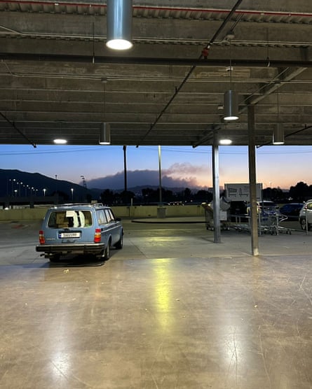 A car sitting alone in a parking garage as an orange glow looms in the distance above hills