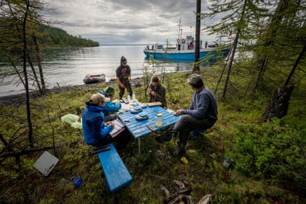 Bir grup araştırmacı, arka planda demirlemiş bir tekneyle göl kıyısında bir piknik masasının etrafında oturuyor