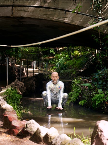 Moby appearing to hover above a stream, wearing a silver space suit