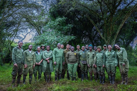 A large group of people, all wearing green uniforms, stand in a field in front of some trees.