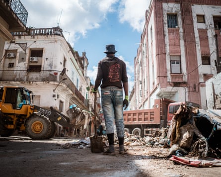 A waste collector watches as a digger removes a large pile of waste from a street corner