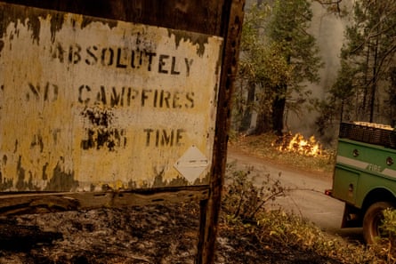 damaged sign saying ‘absolutely no campfires’ in front of a wildfire flames