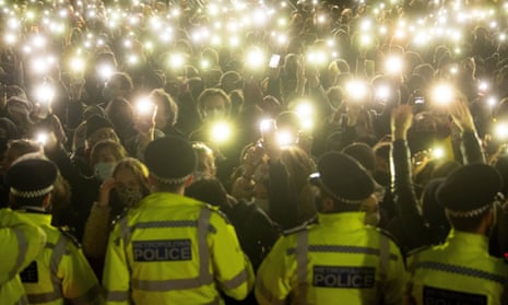 Police face a crowd of people holding up phone torches at Clapham Common vigil