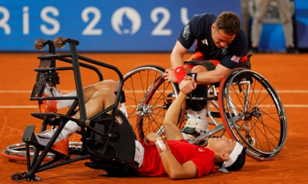 Alfie Hewett leans over in his wheelchair to help Tokito Oda off the clay
