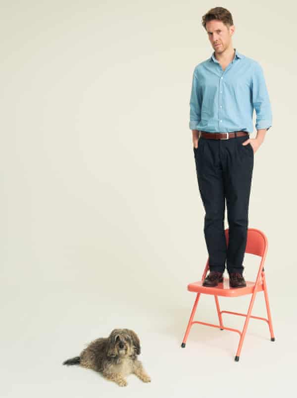 Richard Godwin stands on a chair, a dog sits on the ground