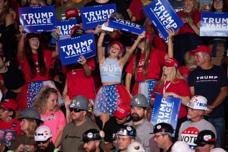 Women dance and cheer in a packed crowd while waving Trump-Vance signs