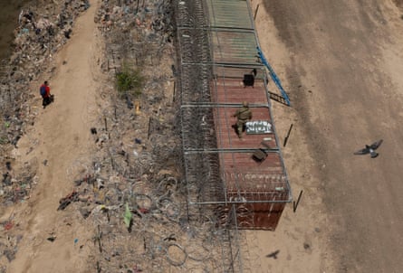 A Texas national guardsman watches over the US-Mexico border atop shipping containers.