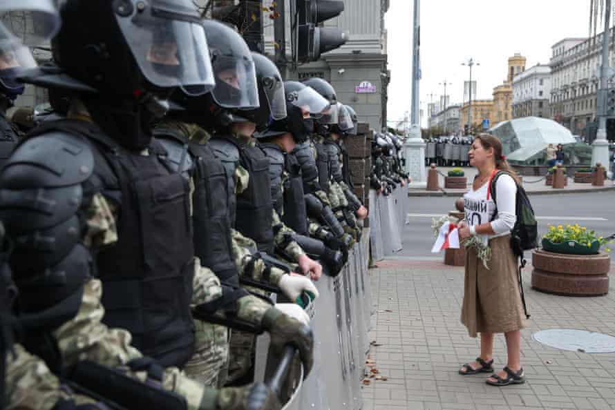 A woman holds flowers and a white-red-white flag as she stands in front of law enforcement officers in Minsk on Sunday.
