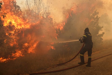 a firefighter aims a hose at a raging wildfire