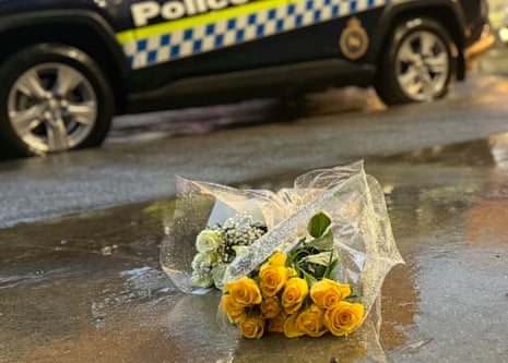 A bunch of yellow flowers on the ground before a police vehicle.