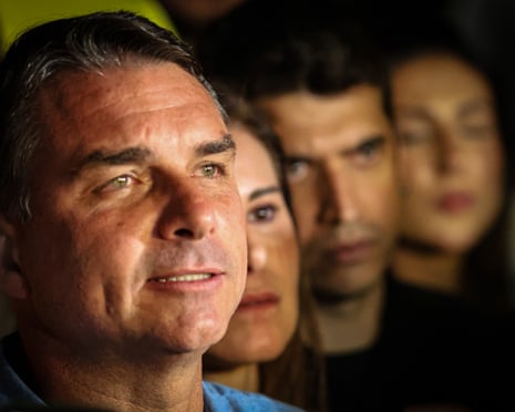 Flavio Bolsonaro looks up with a slight smile as supporters stand blurred behind him