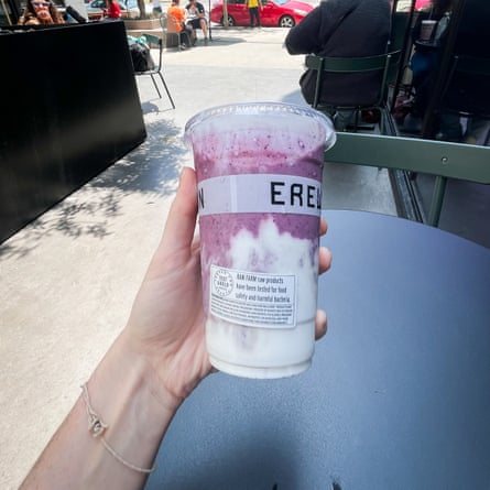A hand holds a pink-and-white swirled smoothie in an Erewhon drink container.