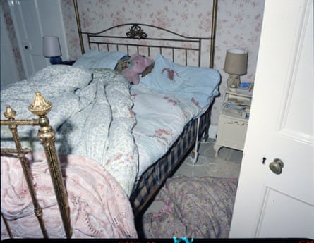 A bedroom with a pink- patterned quily, blue pillowcases and a brass bed. There is blood on the bed linen