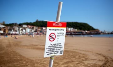A sign on a sunny beach reading: 'Warning: advice against bathing. Poor bathing water quality. The most recent classification is poor, based on samples taken 2018-2022. For more information please scan the QR code'
