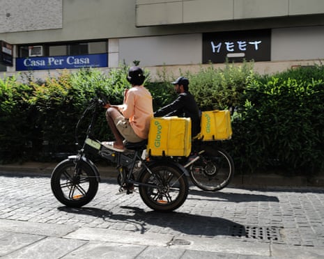 Glovo workers pass by Via Paolo Sarpi in Milan, Italy.