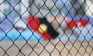 A wire fence in front of an Indigenous flag mural in Darwin