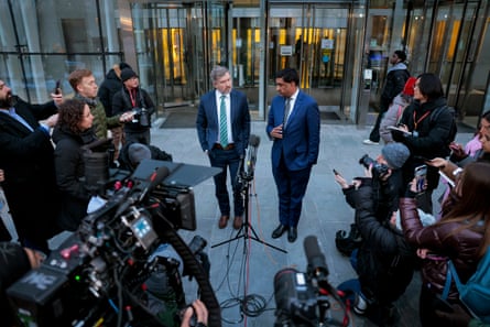 two men speak to people holding cameras