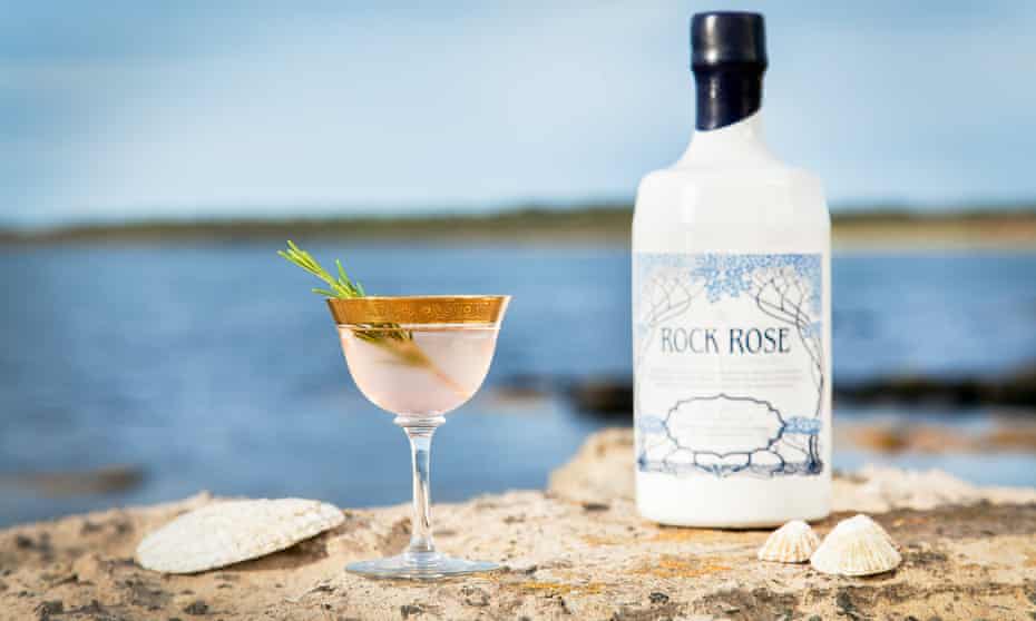 Bottle of Rock Rose gin and a glass of it perched on rocks on the north coast of Scotland. PR image for Dunnet Bay distillery, Scotland.