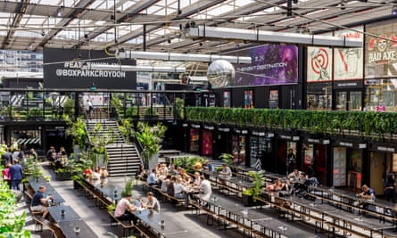 People dining at long benches inside the Boxpark Croydon complex