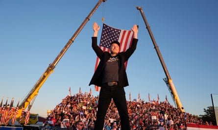 Elon Musk on a stage in front of an American flag at a campaign event for Donald Trump
