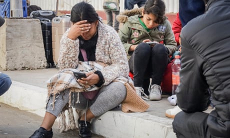 Woman sitting on sidewalk holds head in hand and looks at phone