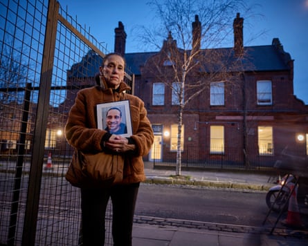 Jude Black looking at the camera, holding a picture of her late son, Joe, while standing across the street from the hostel where he died