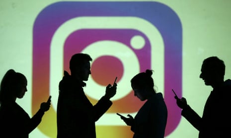 Silhouettes of mobile users are seen next to a screen projection of the Instagram logo