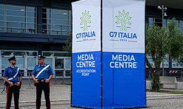 Two police officers standing next to a sign reading the media centre for G7, which is in Italy next week